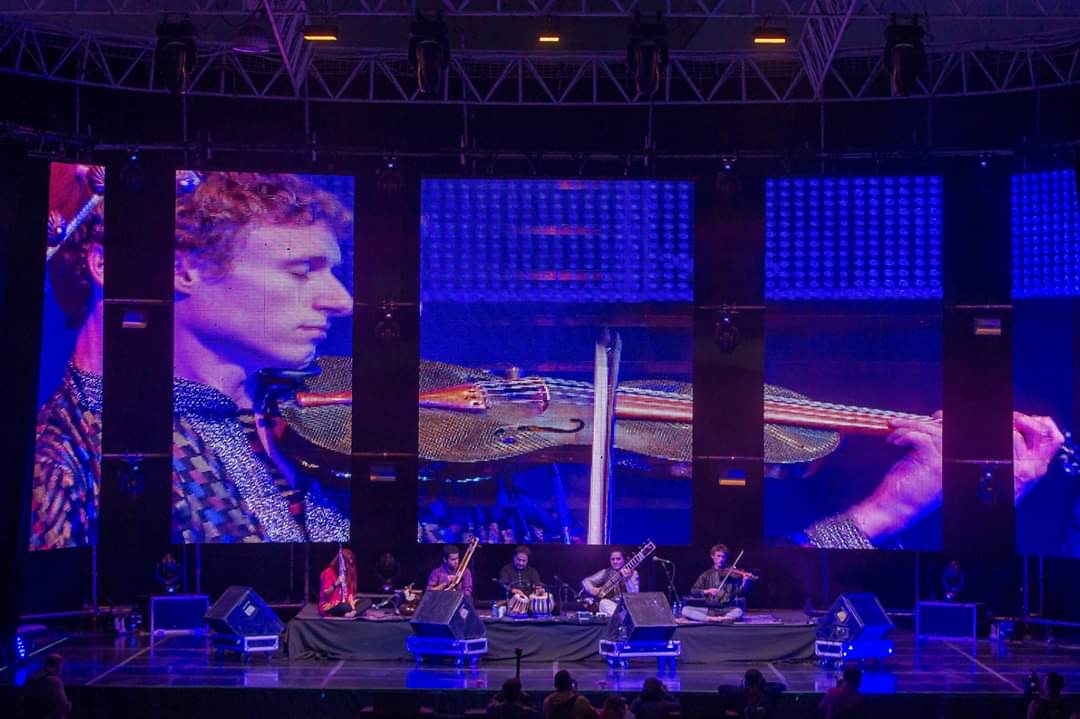 Samuel Wexler performing with an ensemble on a large festival stage in front of a full-height video wall.
