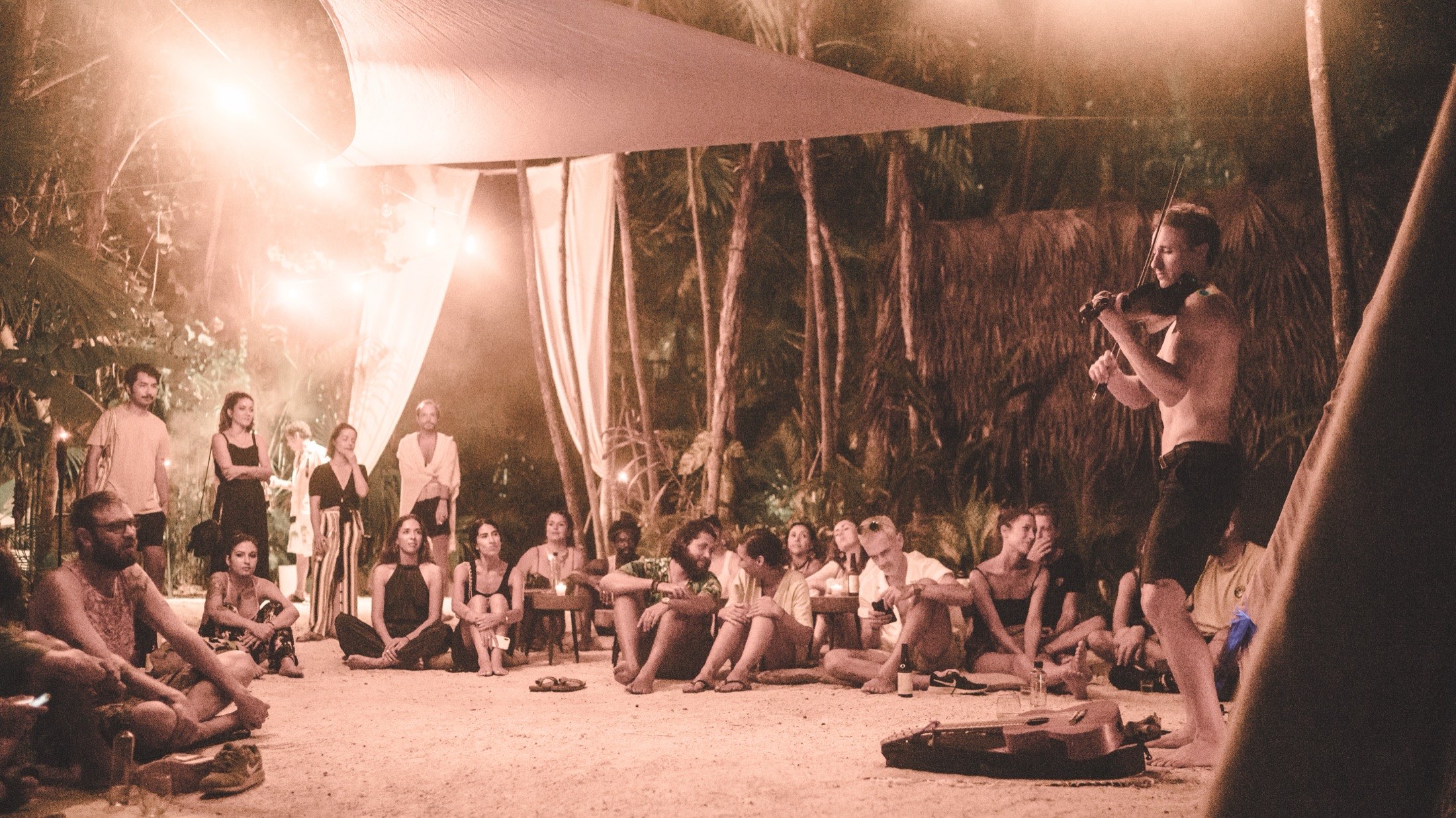 Samuel Wexler live looping by candlelight for a seated audience in a jungle clearing in Tulum.