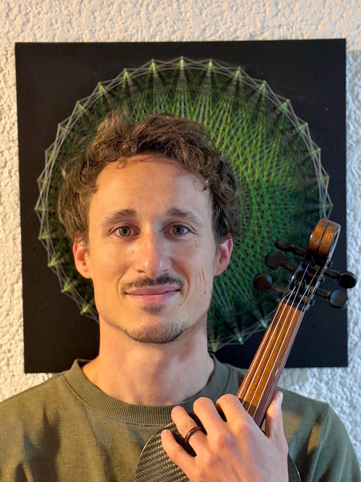 Samuel Wexler holding a mandolin in front of a mandala string artwork.