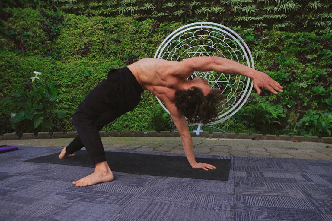Samuel Wexler in a yoga pose on a mat in front of the same Sri Yantra living wall.